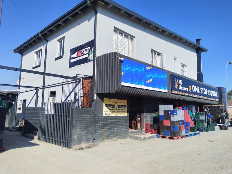 Commercial building exterior featuring a retail storefront with signage, metal security fencing, and a paved entrance area.