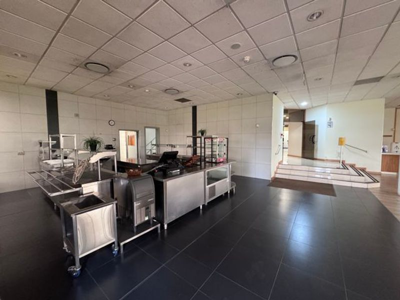 Spacious industrial open-plan area featuring a service counter, suspended ceiling with recessed lighting, and tiled flooring with access to a raised level.
