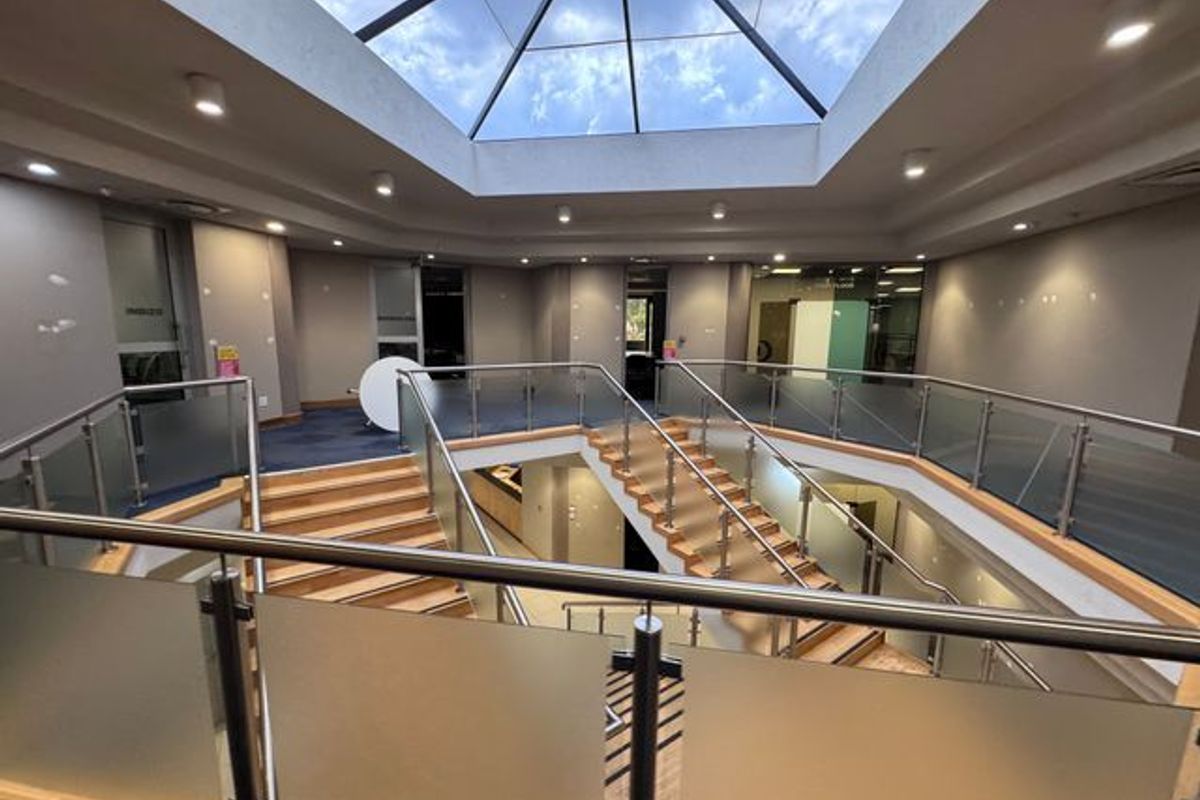 Spacious industrial atrium featuring a large central skylight, modern glass balustrades, and a prominent wooden staircase connecting multiple levels.