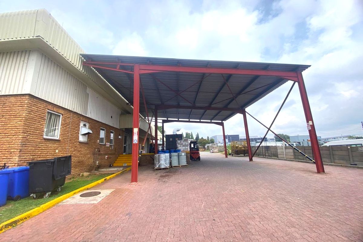 Industrial property featuring a large paved loading area covered by a sturdy steel frame canopy, adjacent to a brick and metal-clad warehouse structure.