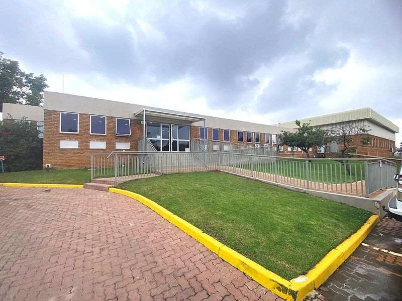 Front exterior view of an industrial building featuring a brick facade, accessible metal ramp, and paved driveway area.