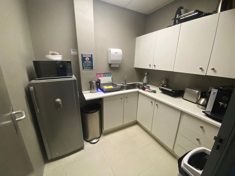 A functional industrial scullery or kitchenette area featuring white built-in cabinetry, laminate countertops, and a stainless steel sink.