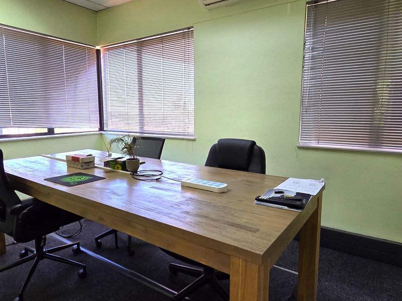 A functional office space featuring carpet flooring, multiple windows with venetian blinds, and a wall-mounted split-system air conditioning unit.