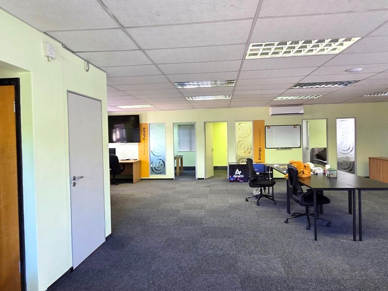 Open-plan office space featuring a suspended ceiling, recessed lighting, carpeted flooring, and multiple internal access points with frosted glass detailing.