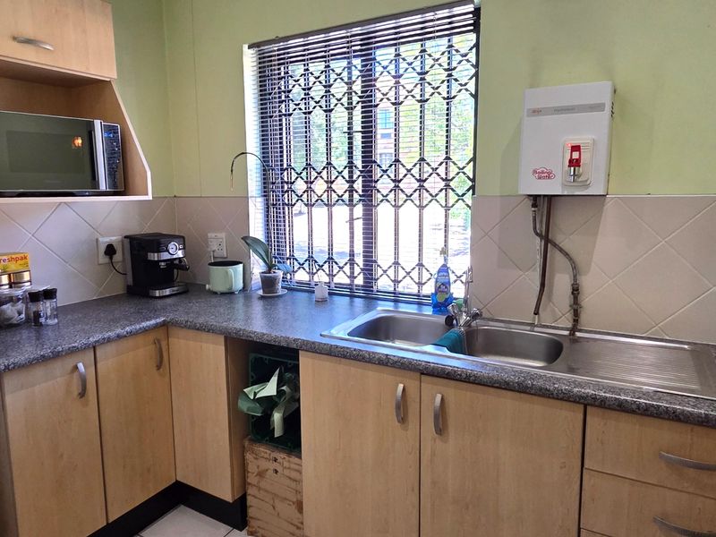 A functional office kitchenette featuring laminate cabinetry, a stainless steel double sink, tiled splashback, and a wall-mounted boiling water dispenser.