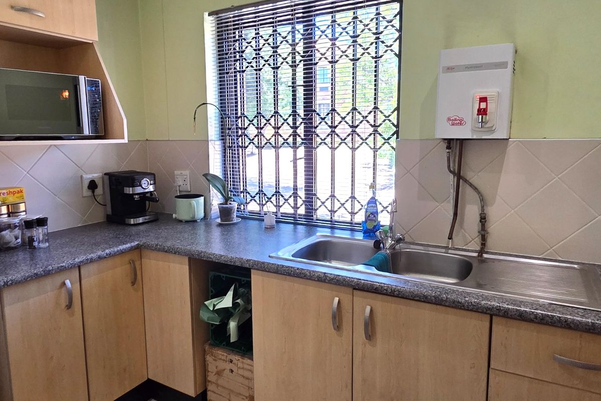 A functional office kitchenette featuring laminate cabinetry, a stainless steel double sink, tiled splashback, and a wall-mounted boiling water dispenser.