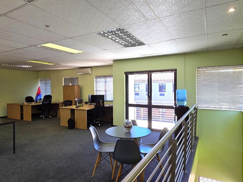 Open-plan office space featuring carpeted flooring, suspended ceilings with recessed lighting, split-system air conditioning, and a metal balustrade overlooking the lower level.