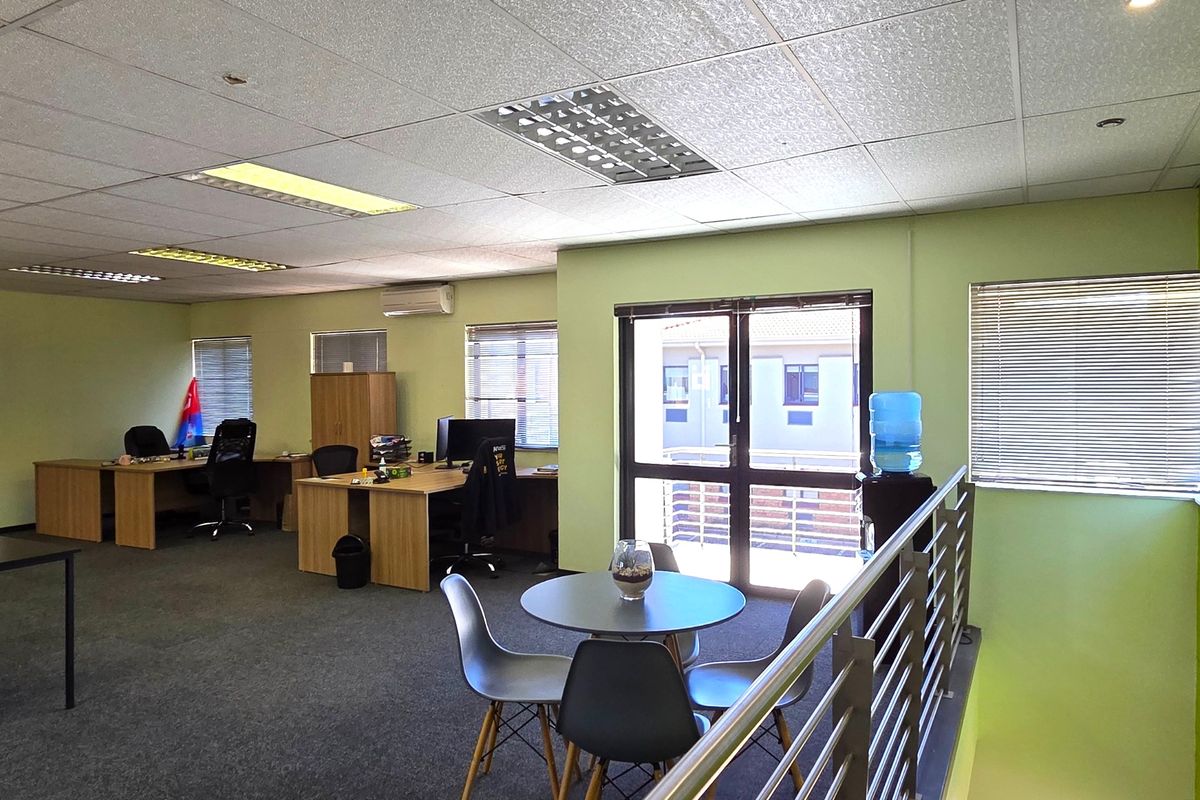 Open-plan office space featuring carpeted flooring, suspended ceilings with recessed lighting, split-system air conditioning, and a metal balustrade overlooking the lower level.