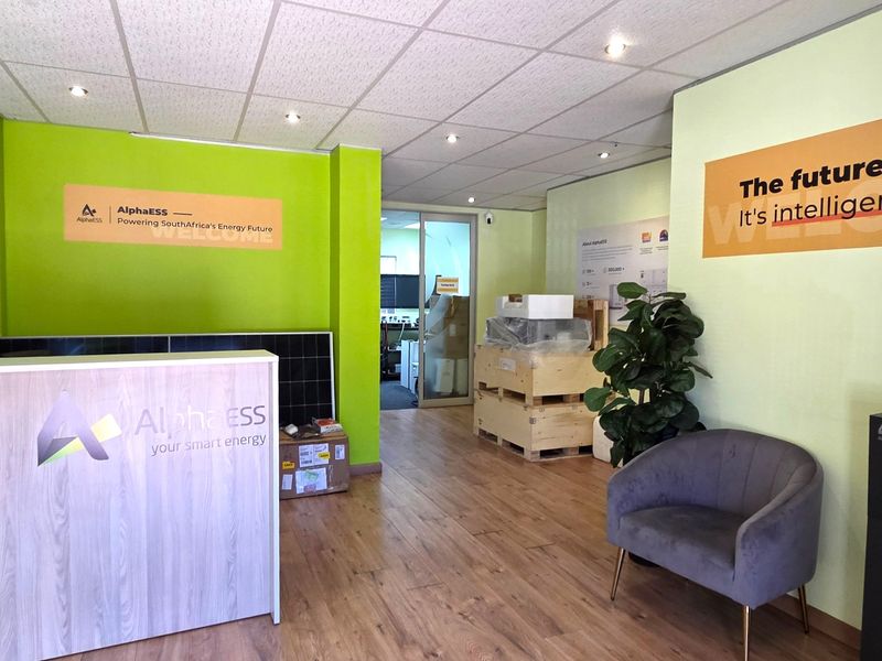 A bright office reception area featuring laminate flooring, recessed ceiling lighting, and a glass partition door leading to the main workspace.