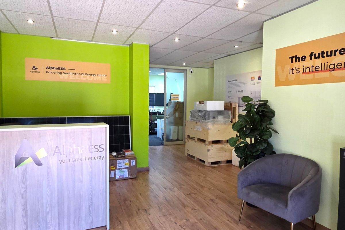 A bright office reception area featuring laminate flooring, recessed ceiling lighting, and a glass partition door leading to the main workspace.
