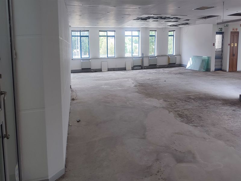 Spacious open-plan office area featuring large windows, air conditioning units, and a suspended ceiling in need of repair and flooring completion.