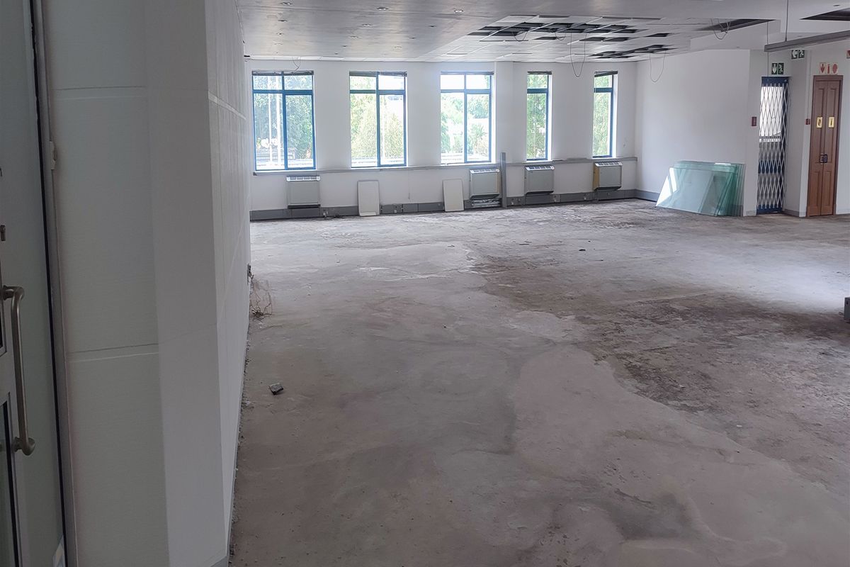 Spacious open-plan office area featuring large windows, air conditioning units, and a suspended ceiling in need of repair and flooring completion.