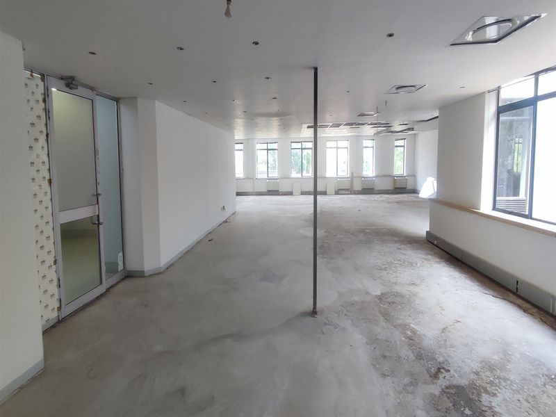 A spacious, vacant office area featuring large windows, recessed lighting, and a central support column, currently requiring flooring and ceiling finish improvements.