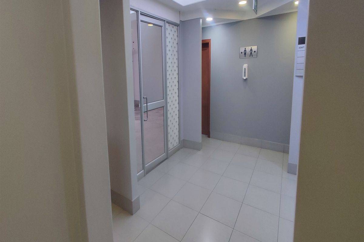 A clean, well-lit office hallway featuring tiled flooring, a skylight, and access to restroom facilities.