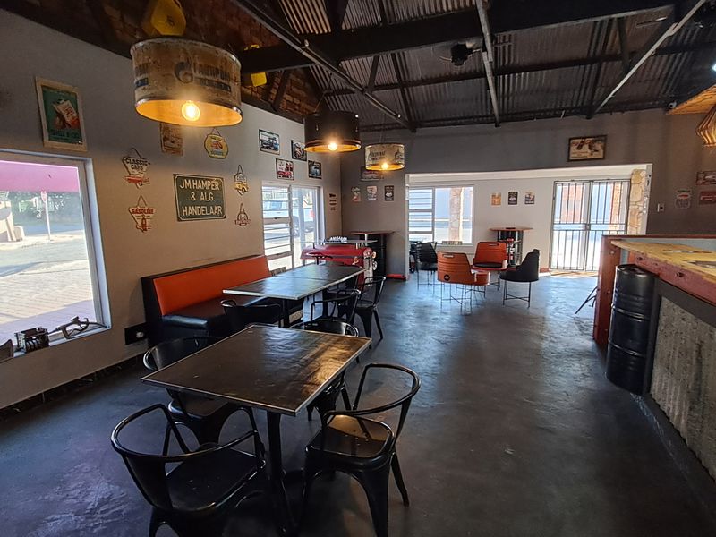 Industrial-style bar area featuring exposed corrugated metal ceilings, brick accents, concrete flooring, and a built-in service counter with integrated lighting.
