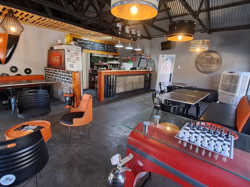 Open-plan commercial space featuring a built-in bar, exposed timber roof trusses, corrugated metal ceiling, and polished concrete flooring with a distinct industrial aesthetic.