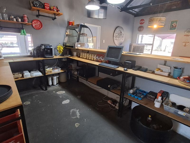 A functional commercial kitchen or service counter area featuring industrial-style shelving, a service sink, and exposed ceiling beams with a casual aesthetic.