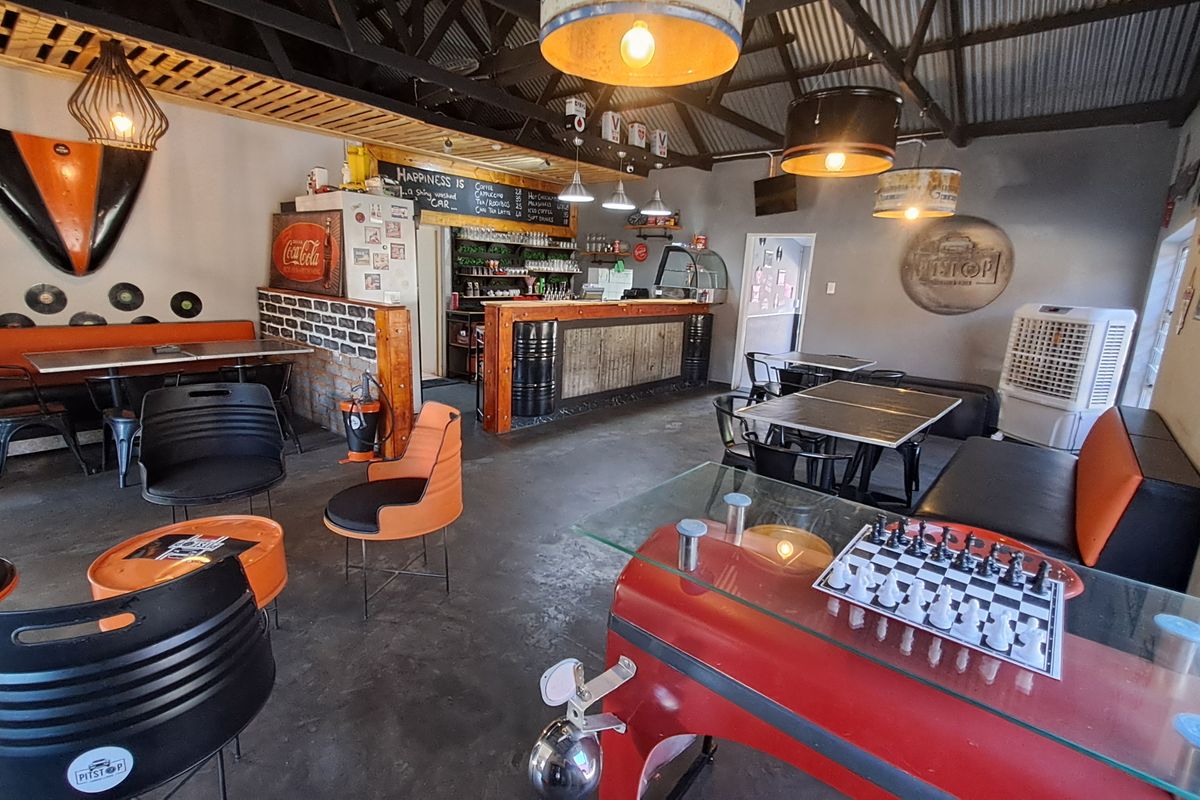 Open-plan commercial space featuring a built-in bar, exposed timber roof trusses, corrugated metal ceiling, and polished concrete flooring with a distinct industrial aesthetic.
