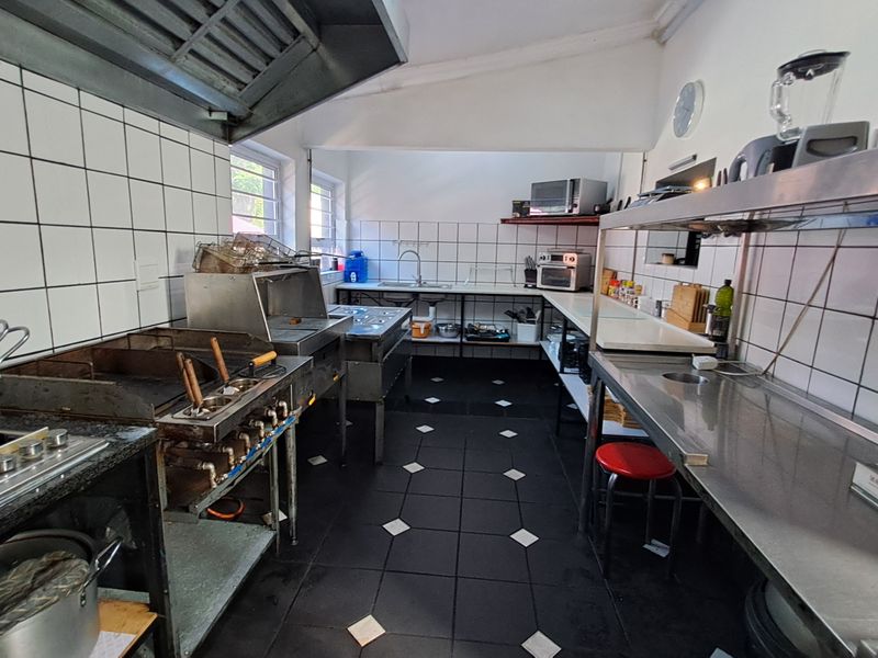 A functional commercial kitchen space featuring stainless steel prep surfaces, a gas griddle, an extractor hood, and tiled wall finishes.