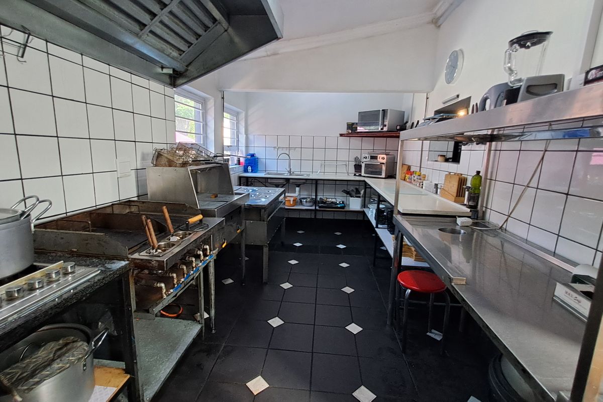 A functional commercial kitchen space featuring stainless steel prep surfaces, a gas griddle, an extractor hood, and tiled wall finishes.