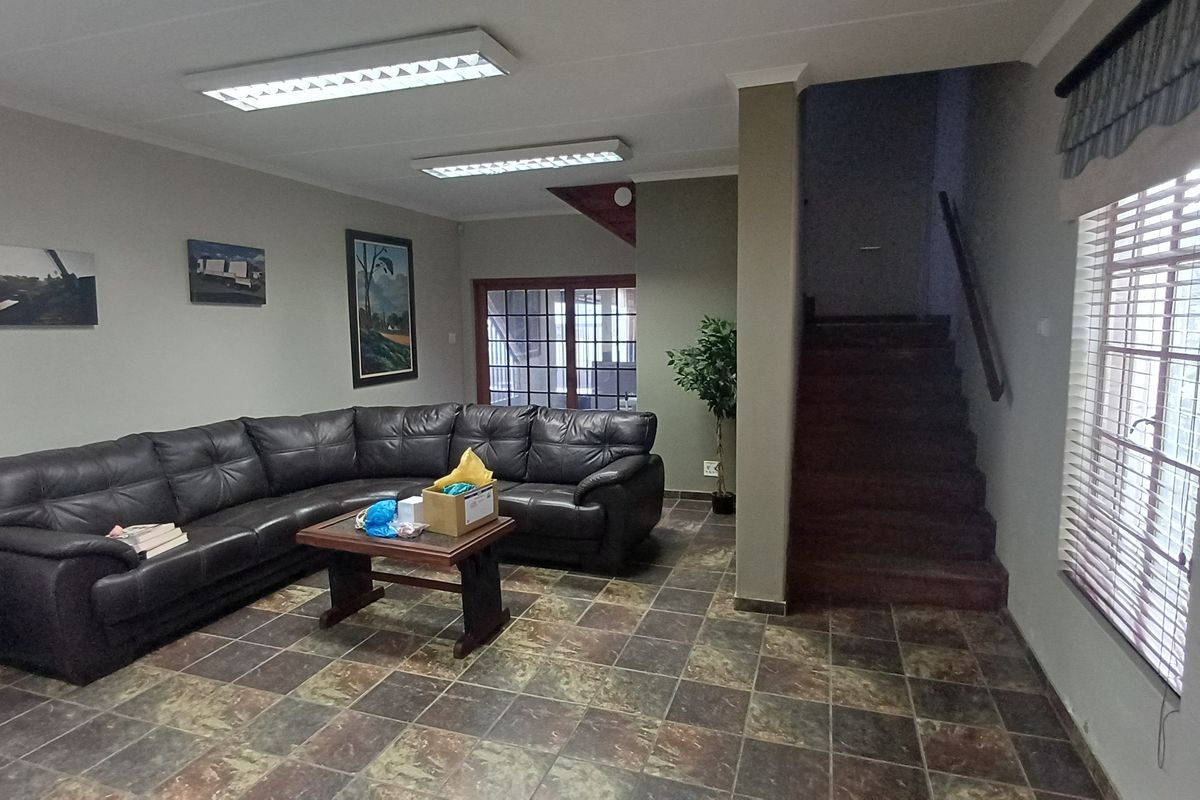 Spacious industrial-style reception or lounge area featuring tiled flooring, recessed fluorescent lighting, and an integrated staircase leading to the upper level.