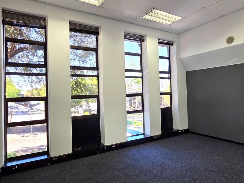 A bright, empty office space featuring large vertical windows, carpeted flooring, and integrated electrical trunking, suitable for a professional workspace.
