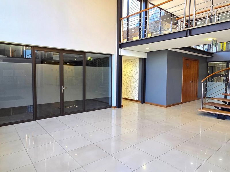 Modern office entrance foyer featuring high ceilings, polished tile flooring, a mezzanine level with steel balustrades, and glass-partitioned office spaces.
