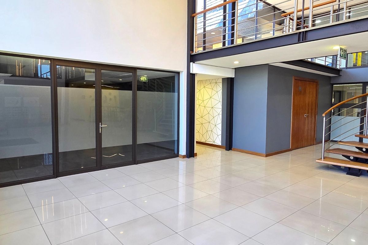 Modern office entrance foyer featuring high ceilings, polished tile flooring, a mezzanine level with steel balustrades, and glass-partitioned office spaces.
