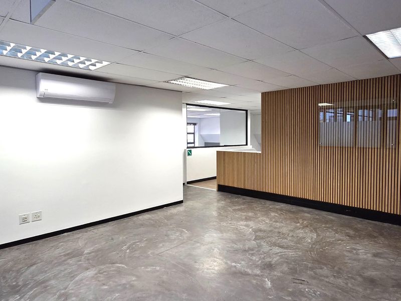Modern open-plan office space featuring polished concrete floors, timber slat feature wall, suspended ceiling with recessed lighting, and a split-system air conditioner.