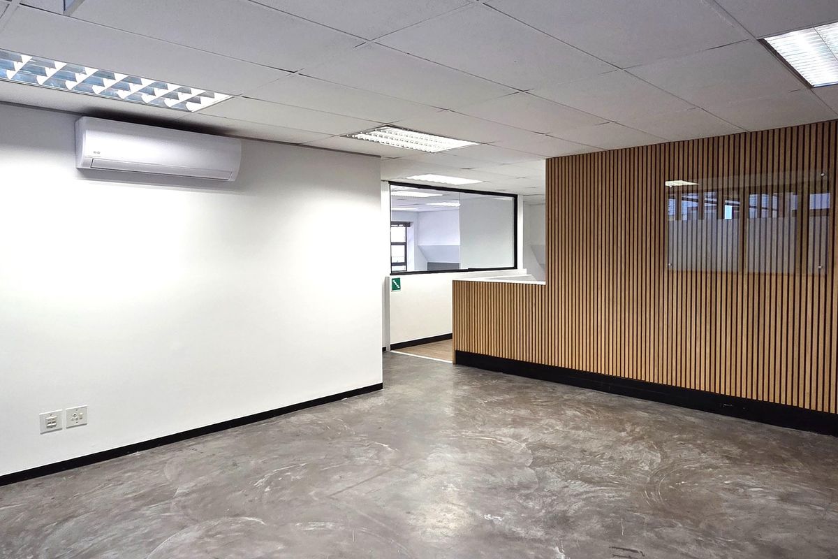 Modern open-plan office space featuring polished concrete floors, timber slat feature wall, suspended ceiling with recessed lighting, and a split-system air conditioner.