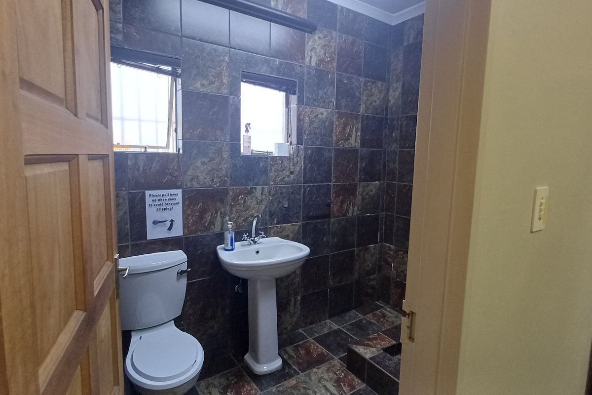 A functional bathroom featuring a pedestal basin, toilet, and dark tiled walls and flooring.
