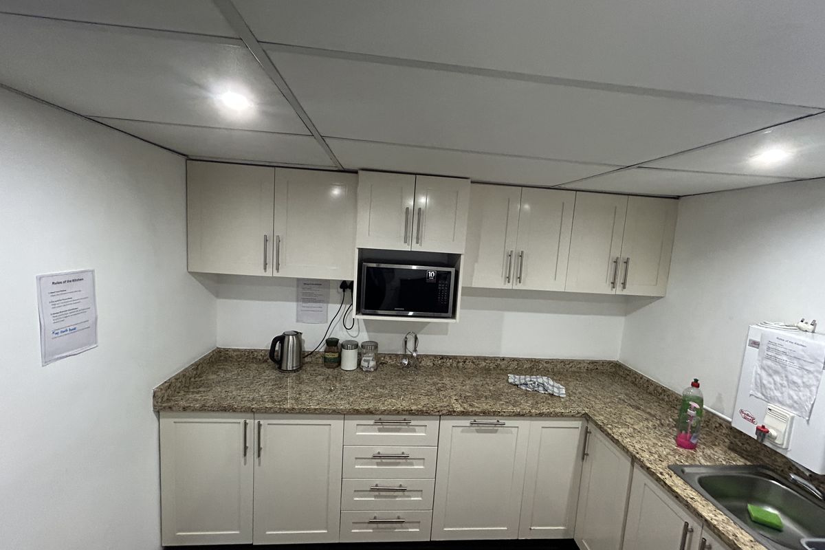 A functional office kitchenette featuring granite countertops, ample laminate cabinetry, a built-in microwave, and a stainless steel sink with a drop ceiling.