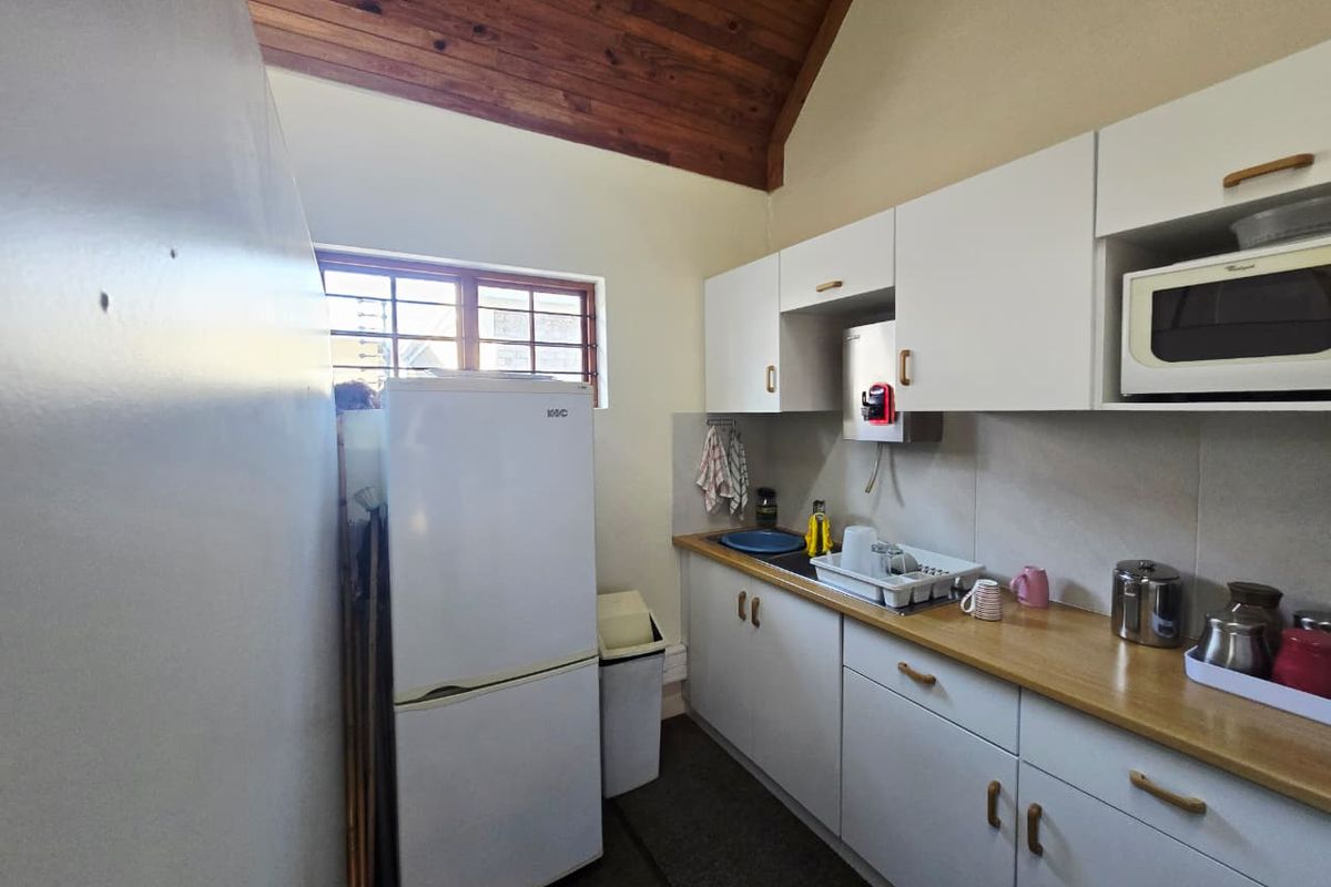 A compact kitchen featuring white cabinetry, a timber vaulted ceiling, and a functional layout with built-in microwave and sink area.