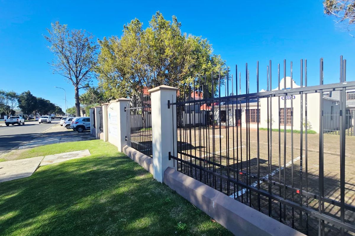 Front exterior view of the office property featuring a paved parking area secured by metal fencing and masonry pillars.