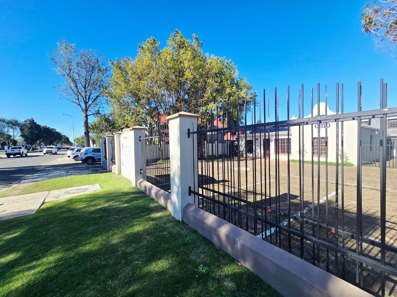Front exterior view of the office property featuring a paved parking area secured by metal fencing and masonry pillars.