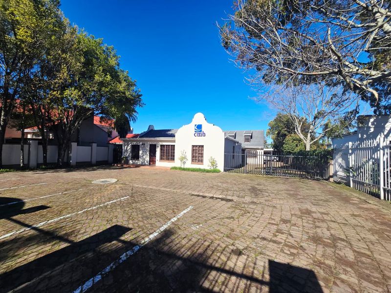 Front view of the office property featuring a paved parking area, secure gated entrance, and a distinctive gabled building facade.