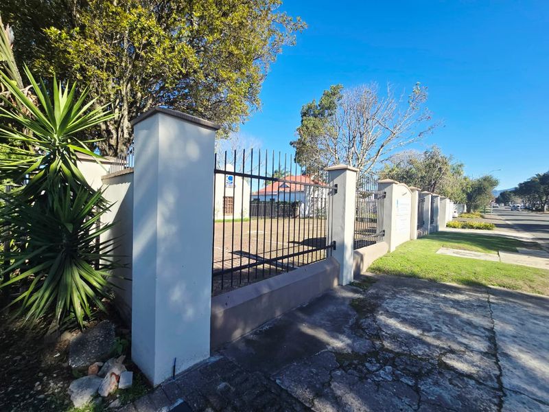 Front view of the office property featuring a secure wrought iron fence with masonry pillars and a paved driveway area.