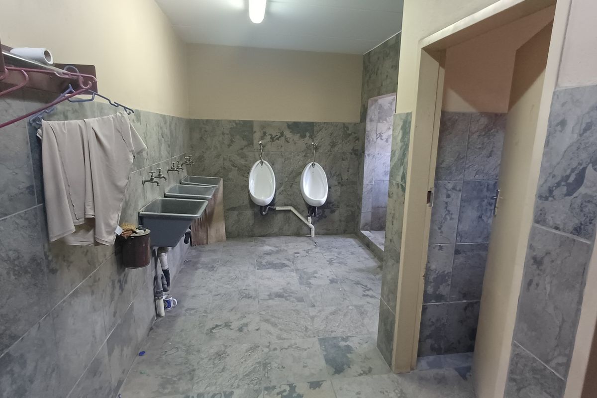 Industrial washroom facility featuring multiple wall-mounted urinals and utility sinks with tiled wall and floor finishes.
