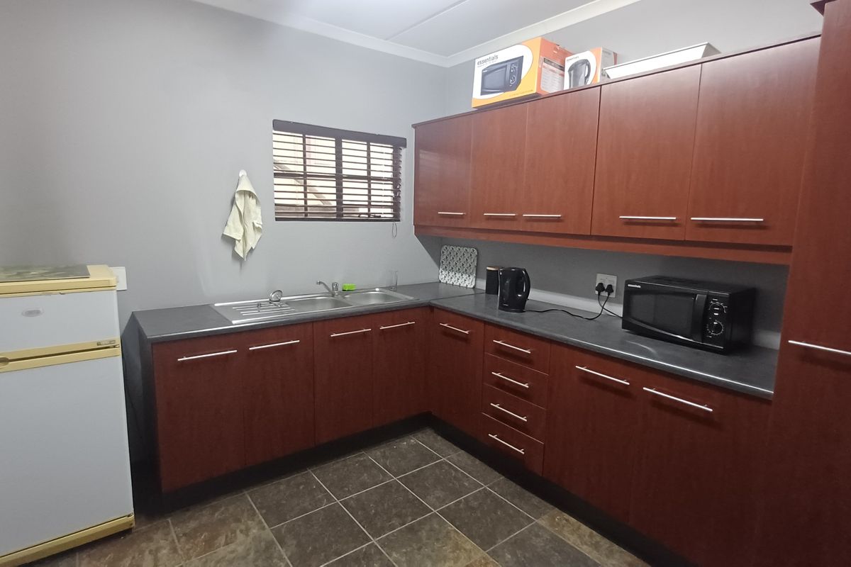 A functional kitchen area featuring dark wood-toned cabinetry, dark countertops, a stainless steel sink, and tiled flooring.