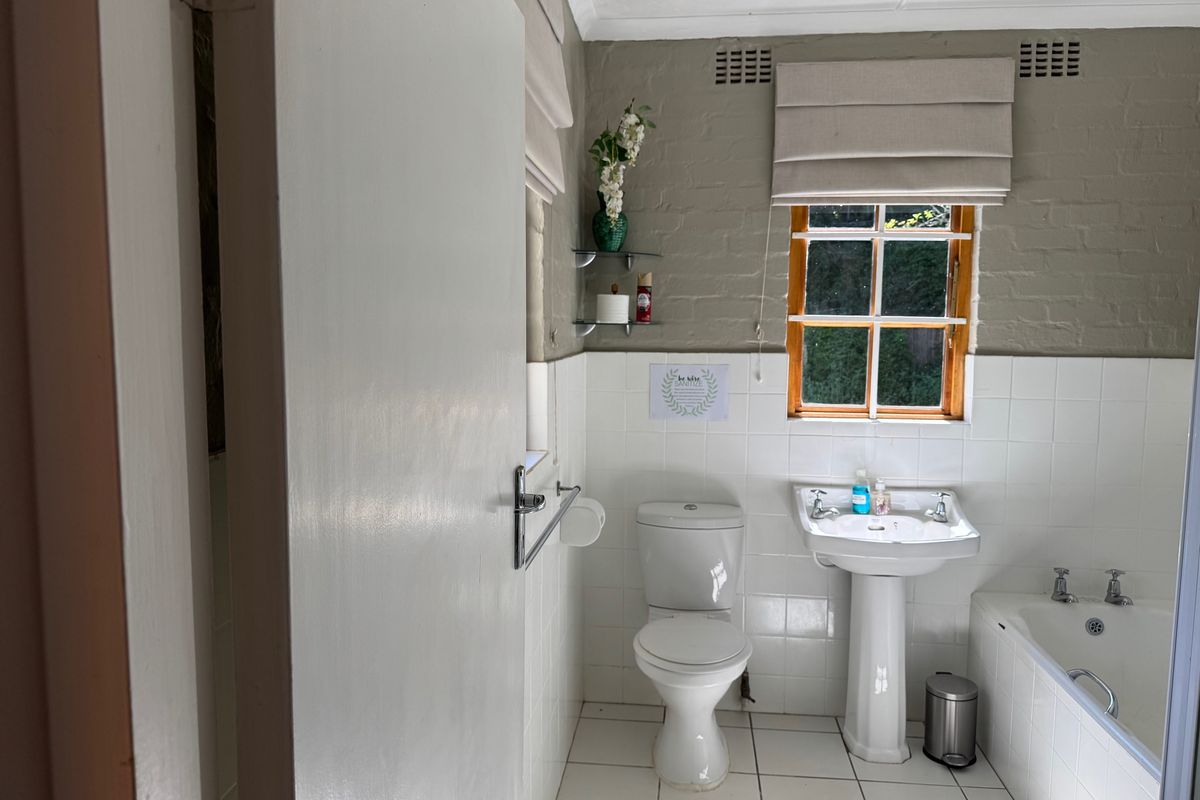 A functional bathroom featuring a pedestal basin, standard toilet, and a built-in bathtub with tiled splashbacks and a window for natural light.