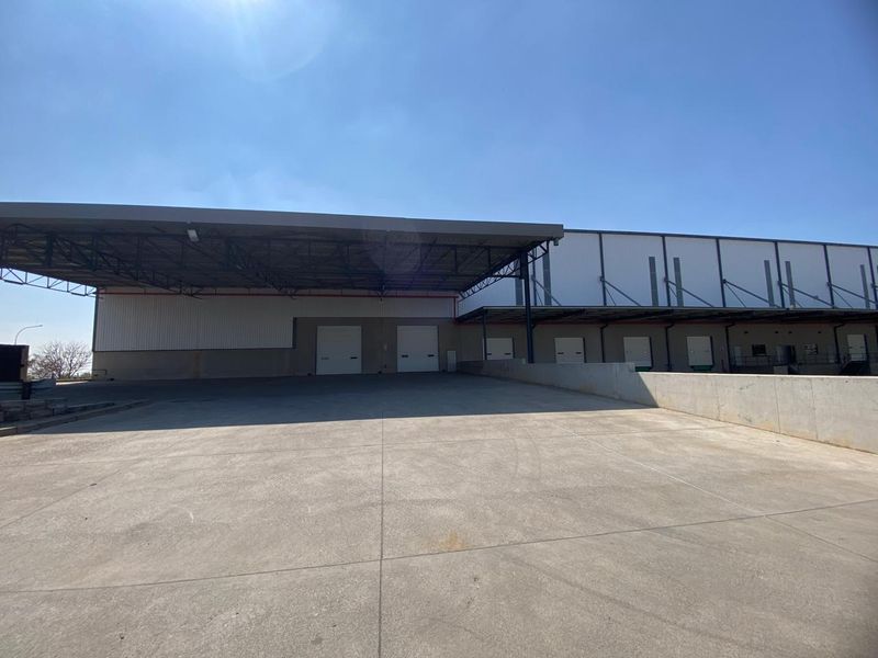 Industrial warehouse exterior featuring a large concrete loading yard, steel canopy, and multiple roller shutter doors for efficient logistics and distribution operations.