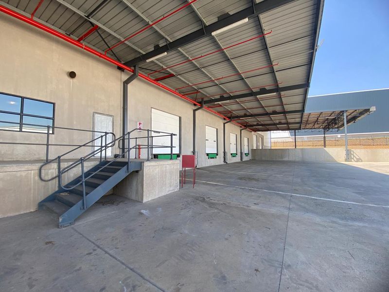 Industrial loading bay area featuring multiple dock levelers, a large steel canopy, fire sprinkler infrastructure, and a spacious concrete hardstand for logistics operations.