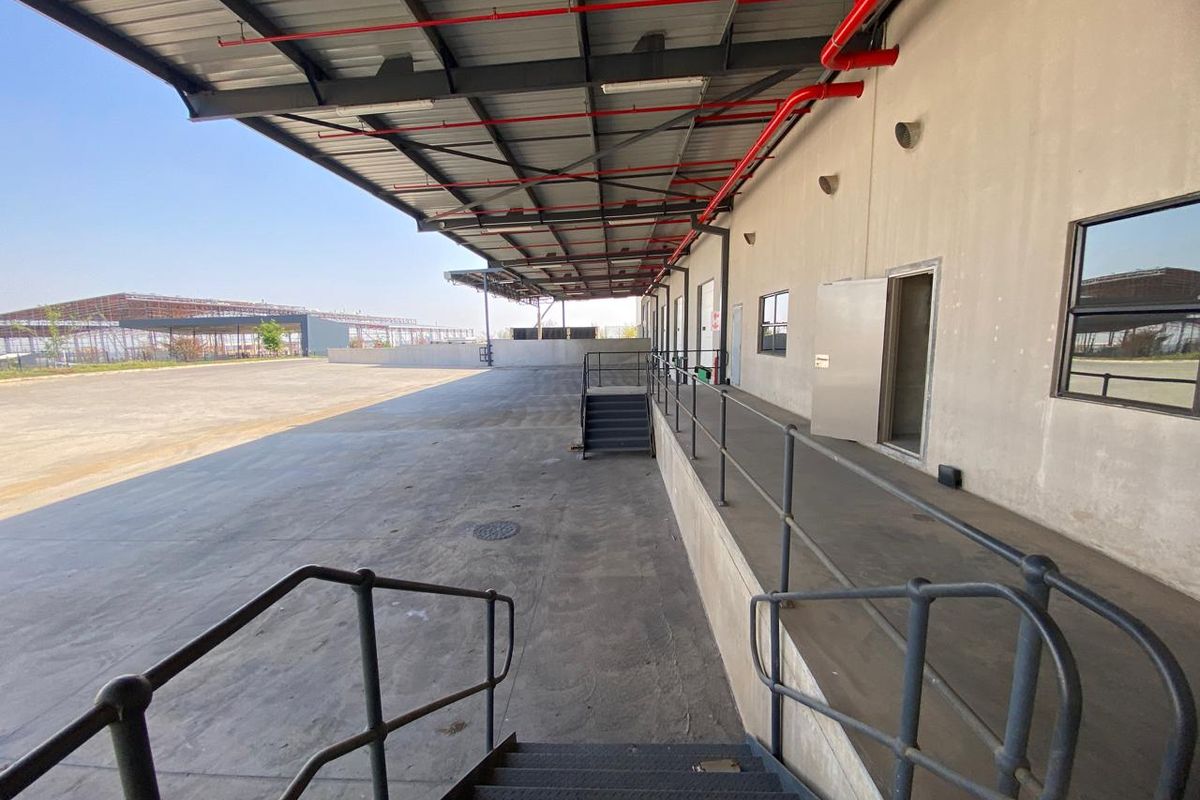 Industrial loading bay area featuring a large concrete apron, covered loading dock with metal canopy, and steel access stairs.