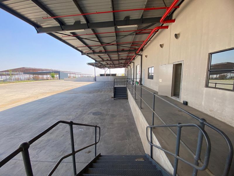 Industrial loading bay area featuring a large concrete apron, covered loading dock with metal canopy, and steel access stairs.