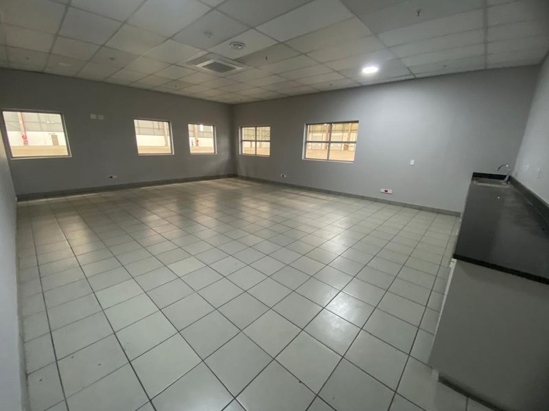 Spacious open-plan industrial office area featuring tiled flooring, a suspended ceiling, and a built-in kitchenette counter with a sink.