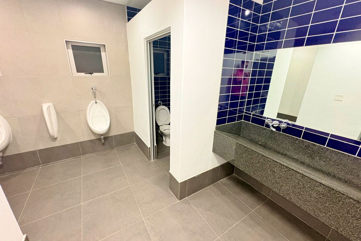 A clean, modern commercial bathroom featuring wall-mounted urinals, a granite trough sink with wall-mounted faucets, and a private enclosed toilet cubicle.