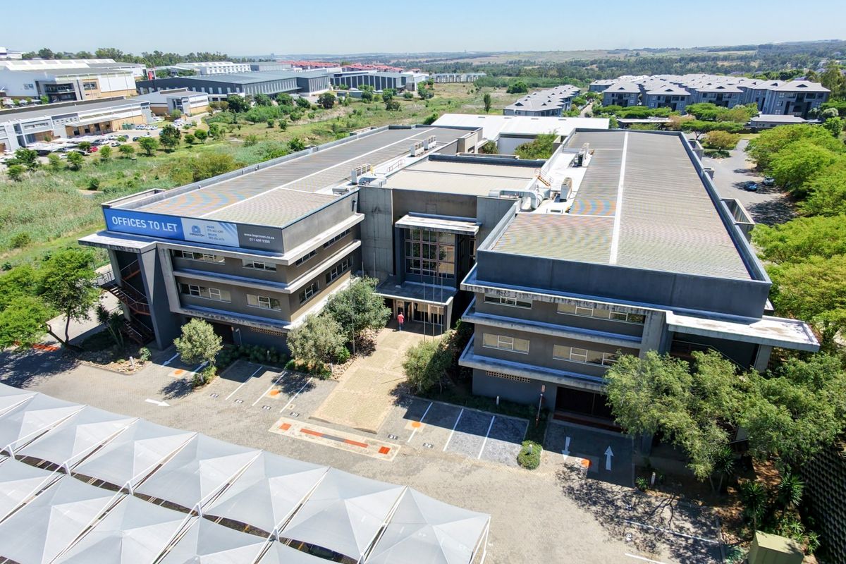 Aerial view of a modern multi-story office complex featuring extensive paved parking, shade cloth carports, and well-maintained landscaped surroundings.
