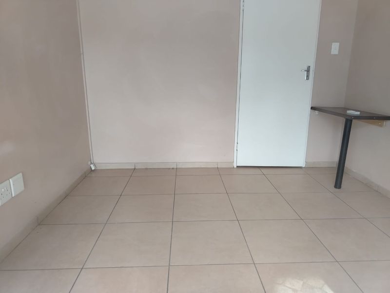 A clean, empty office space featuring neutral tiled flooring, a wall-mounted desk, and standard electrical points, ready for professional use.