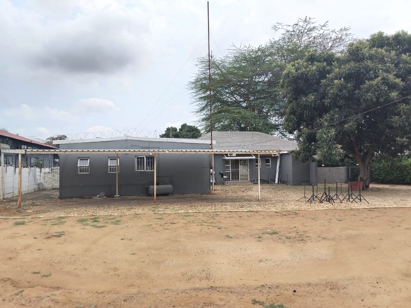 Rear view of the property featuring a covered patio area, paved section, and security fencing surrounding the building perimeter.