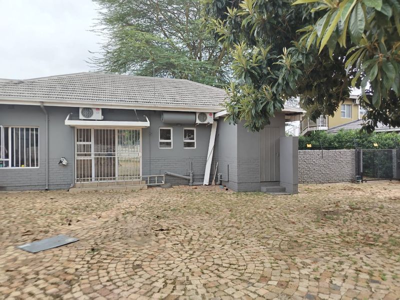 Rear exterior view of the property featuring a paved courtyard, brick facade, security gates, and mounted air conditioning units.